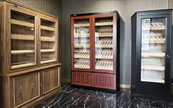 Three large cabinet humidors in walnut and dark finishes in a marble-floored showroom